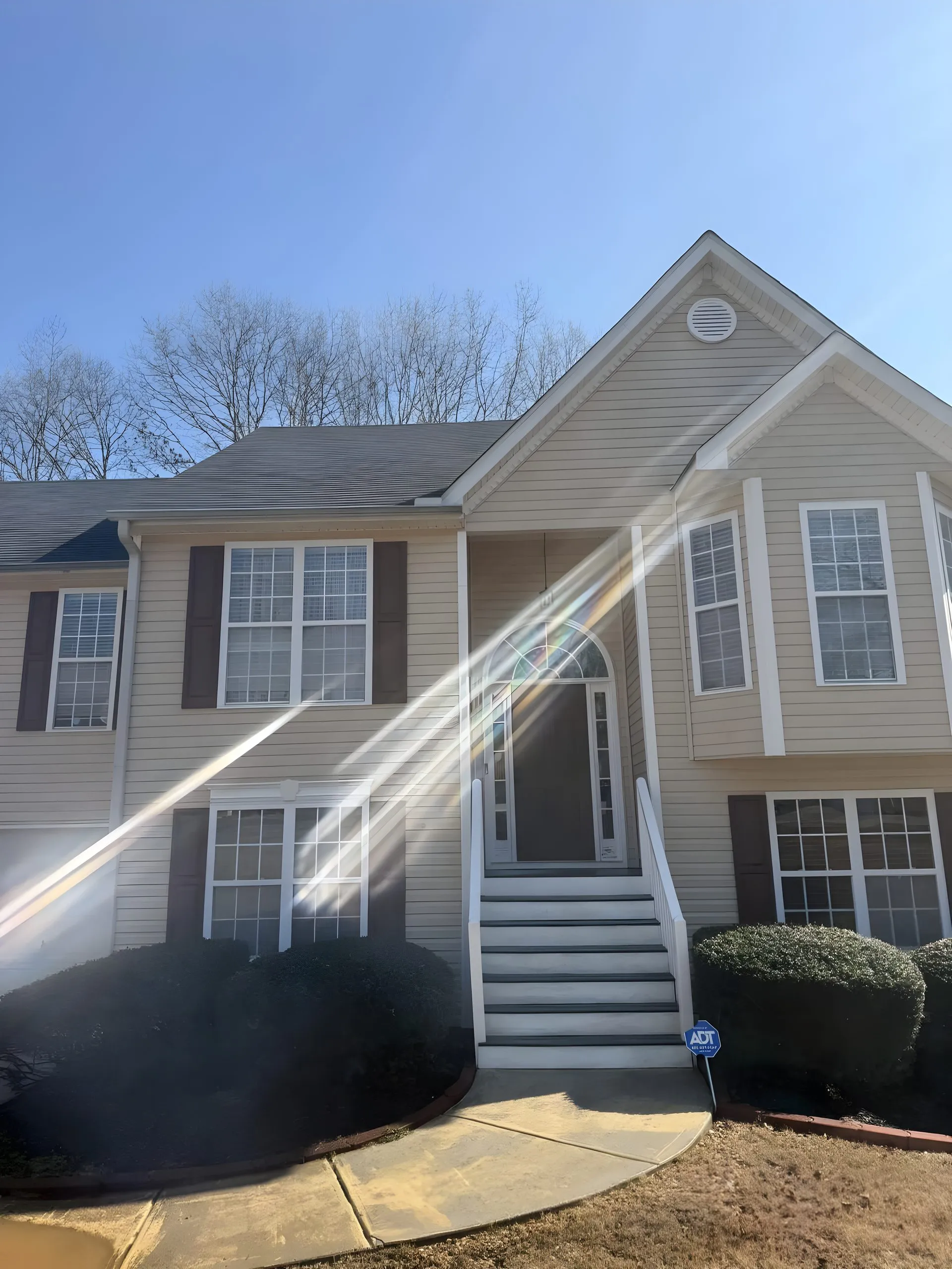 Sunlit two-story tan home in Villa Rica with clean siding, sun rays across the front after a house wash