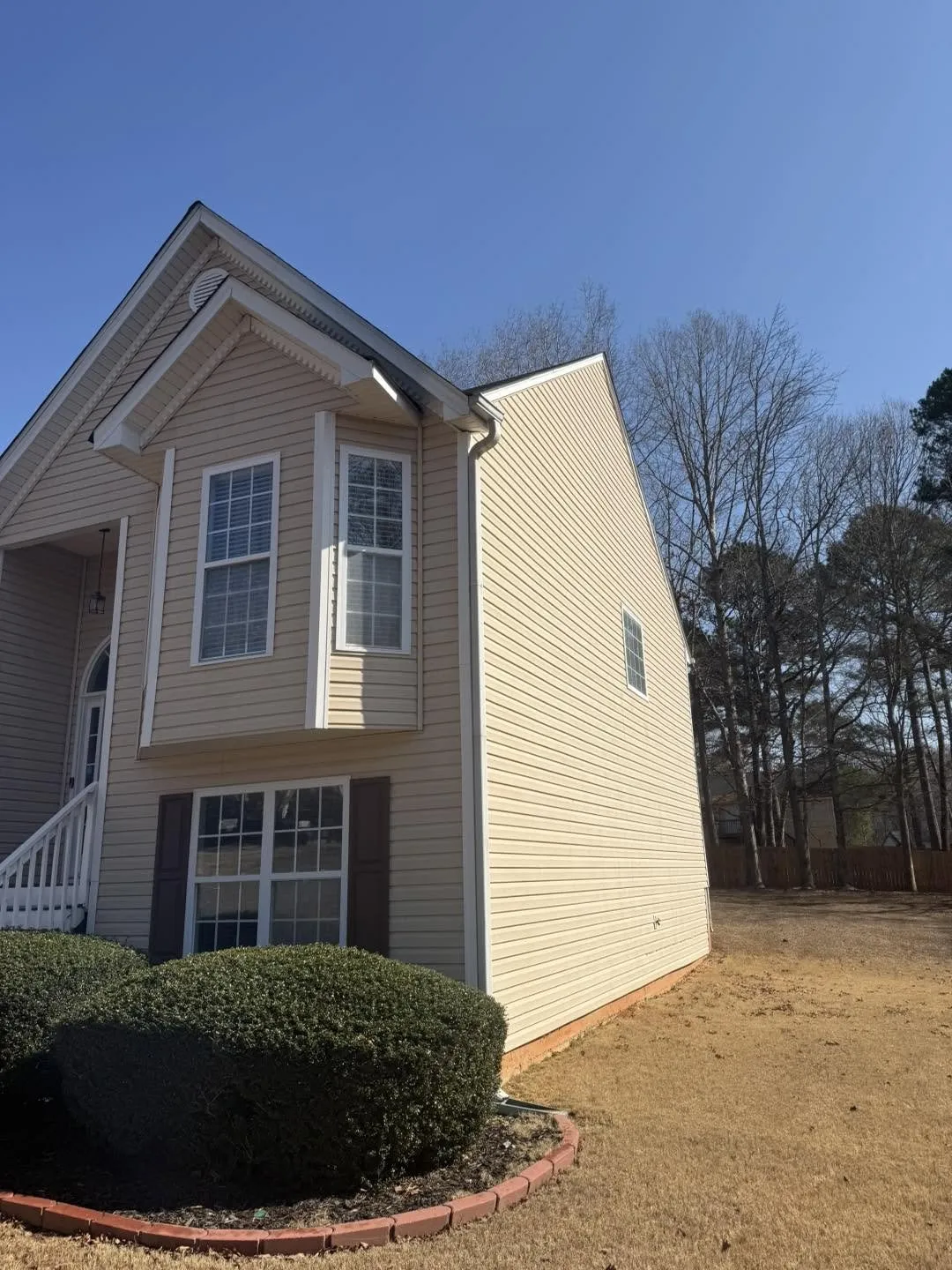 Corner view of a two-story tan home in Villa Rica with brown shutters, a bay window and clean siding against a blue sky