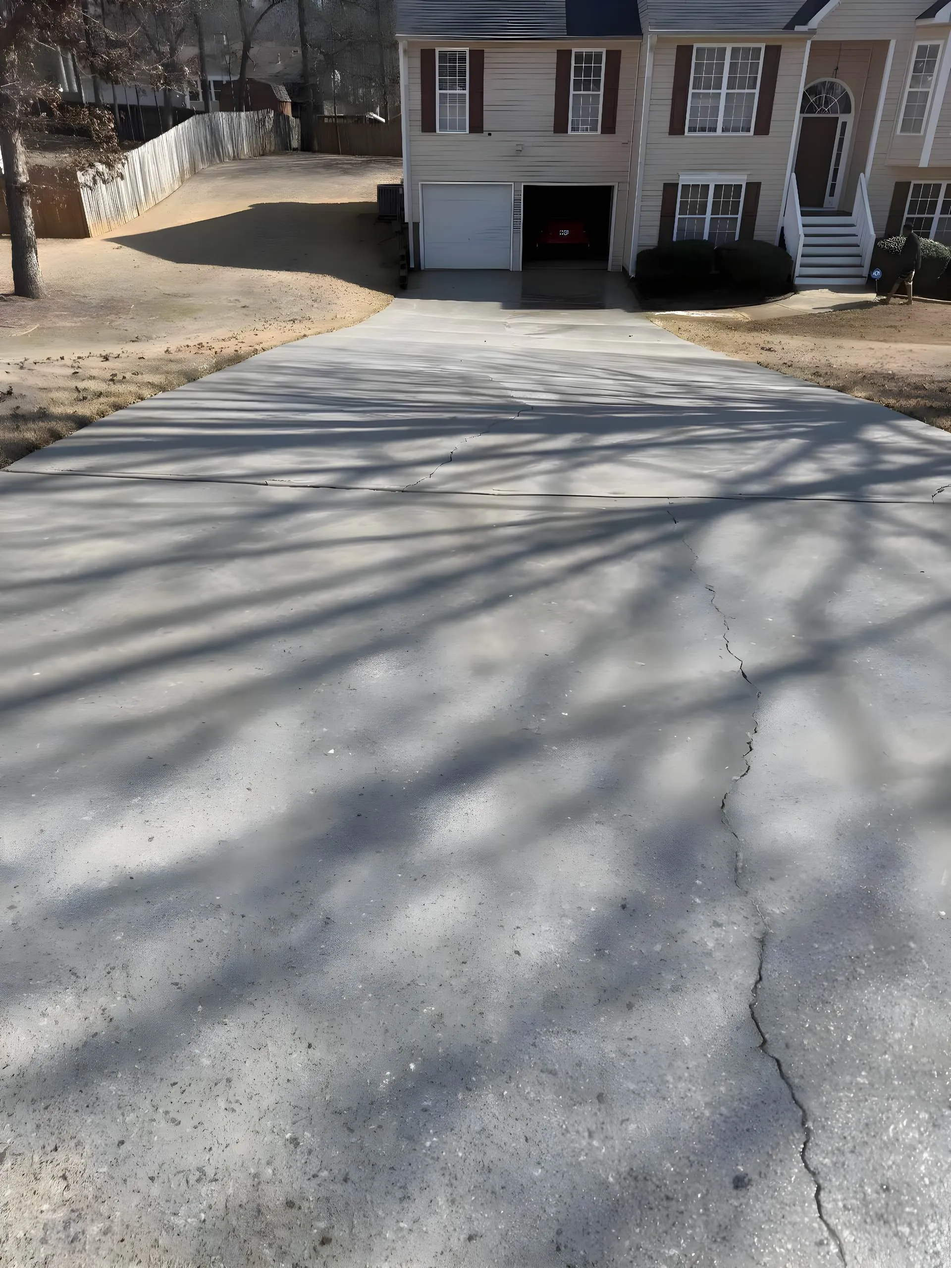 Split-level home driveway in Villa Rica crossed with long tree shadows, a hairline crack running down its length