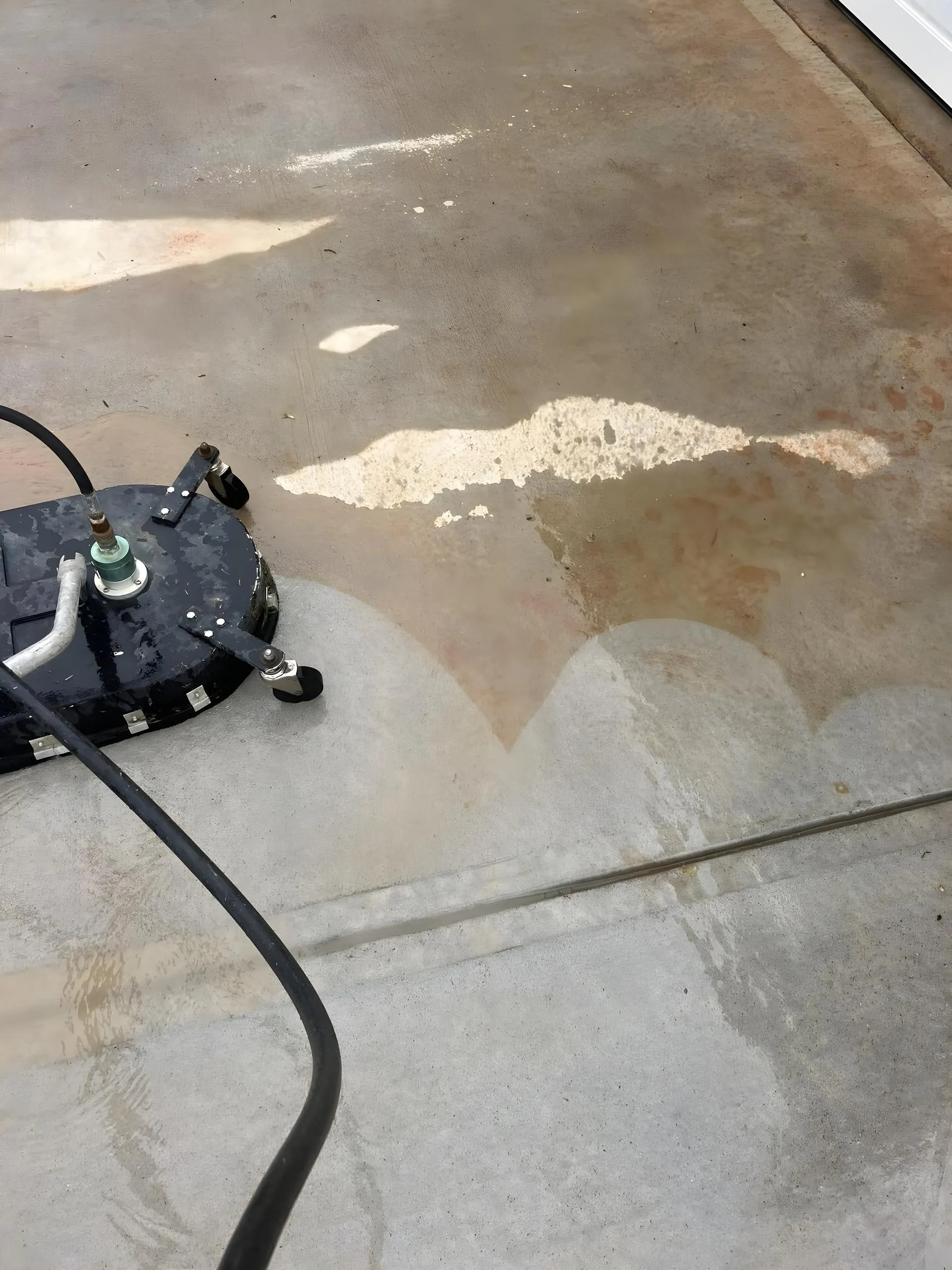 Surface cleaner mid pass, clean scalloped arcs cut through rust-stained concrete