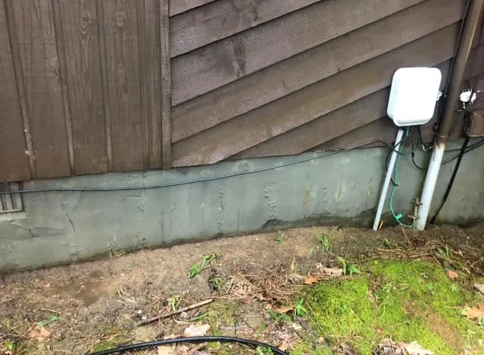 The same foundation wall and utility box, algae gone, clean grey concrete after pressure washing